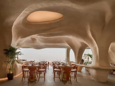 A modern restaurant with concrete walls and ceiling, featuring round tables and high chairs.