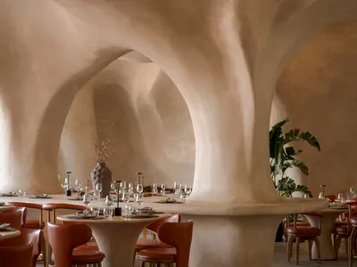 A contemporary restaurant interior with textured, concrete columns and minimalist furniture.