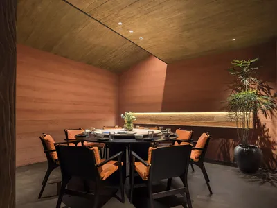 Unusual ceiling slant, exposed light beams, industrial-style round wooden dining table surrounded by orange padded chairs, co