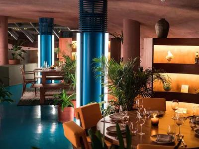 A modern restaurant interior with metallic columns, indoor greenery, and round tables.
