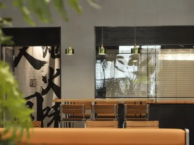 A modern restaurant interior with minimalist decor, wooden tables, pendant lights, and contemporary furniture.