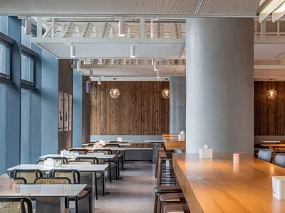 Modern, minimalist restaurant interior with wooden tables, concrete walls, and glass pendant lights.