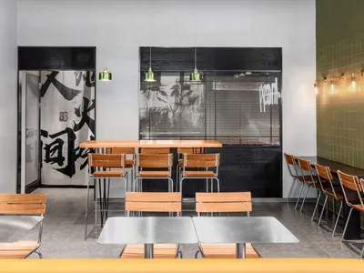 Modern minimalist restaurant interior with wooden tables, metal chairs, concrete flooring, and industrial lighting.