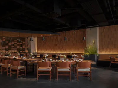 A modern restaurant interior with wooden tables, concrete flooring, and industrial lighting.