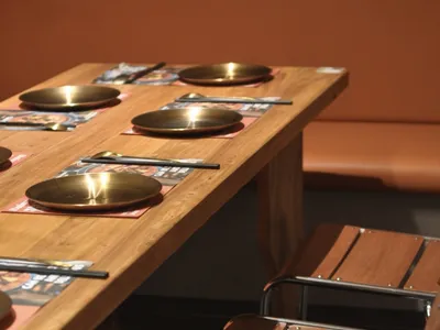 A modern restaurant interior featuring wooden benches and metal-frame chairs, placed at a wooden dining table.