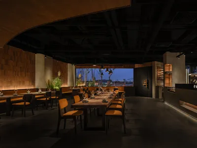 A modern restaurant interior featuring wooden tables, concrete walls, and plant life