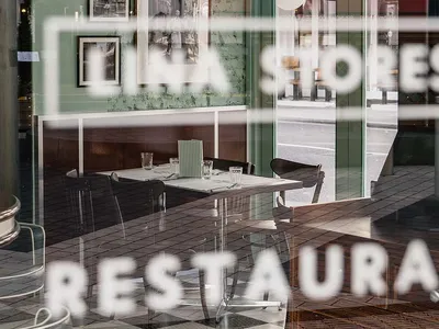 Cafe interior with wooden walls and checkered tiled floor, featuring a dining table and chairs.