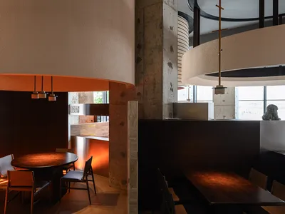 Modern industrial restaurant interior with wooden tables and chairs, concrete walls, and circular pendant lights.