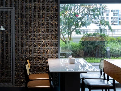 A restaurant interior with a metal grid wall behind a table, featuring pebbles embedded in a concrete wall.