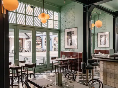 Modern restaurant interior with black and white tiled floor, green walls, and industrial lighting.