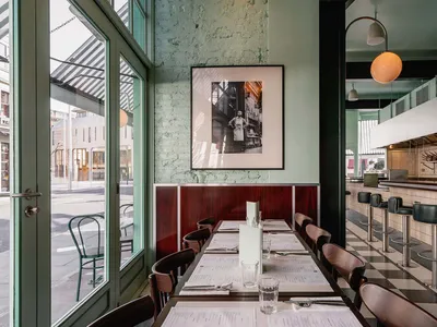 Modern restaurant interior with tables, chairs, and a kitchen counter.
