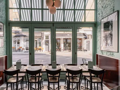 A modern restaurant interior with black chairs, large windows, and metal and glass features.