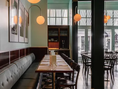 Modern, minimalist restaurant interior with wooden tables, glass walls, metal accents, and upholstered seating.
