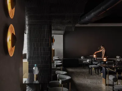 An industrial-style restaurant bar with exposed brick walls, metal chairs, and round tables.