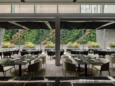 Modern minimalist restaurant interior with marble tables, black stone and chairs, and a living wall.