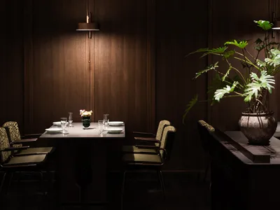 Modern restaurant interior with dark wooden walls and furniture, featuring a dining table set for four with white plates and