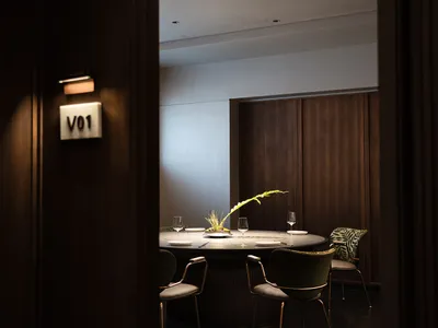A modern, private dining room with wooden walls, a round table, and green chairs.