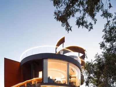 A modern restaurant exterior illuminated at night, featuring metal cladding and curved glass.