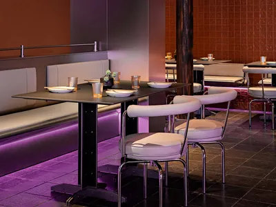 Industrial-style restaurant interior featuring purple backlit seating and dark tile floor.
