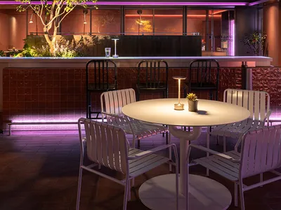 Outdoor seating area of a modern restaurant with metal tables and chairs under illuminated lighting fixtures.