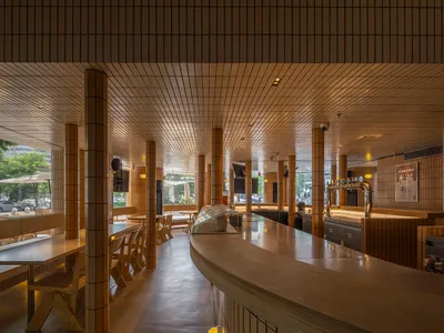 Interior view of a modern restaurant bar with tile walls, cement floor, and rectangular bar counter.