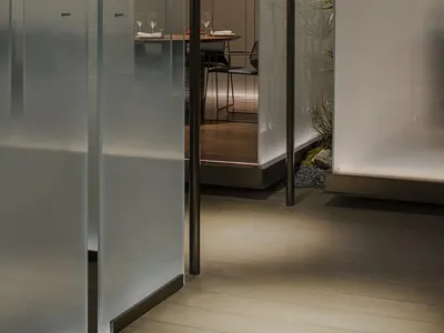 Modern restaurant private dining room with glass walls, wooden floor, and decorative plants.
