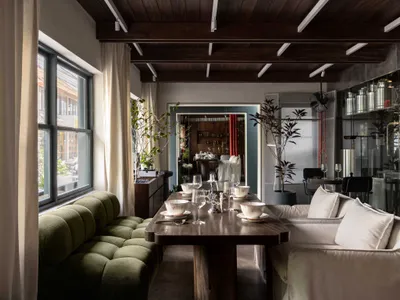 An industrial-style restaurant interior with wooden furniture, white cushions, and green plants.