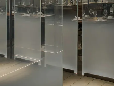 A modern restaurant interior with glass and concrete surfaces, featuring minimalist decor and a spacious layout.