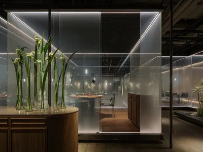 Modern restaurant with a glass privacy panel, featuring a wooden table setting and plants.