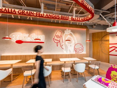 Modern fast food cafe with contemporary design elements, including wooden benches, white tables, and red lighting.