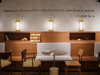 Modern cafe interior featuring wooden furniture and white seats with a dark wooden floor and textured wall