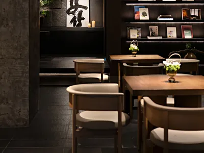 A modern cafe interior with wooden tables, fabric chairs, and concrete walls.