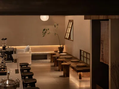 A minimalist restaurant interior featuring wooden furniture and a warm, inviting ambiance with soft lighting and a single pla