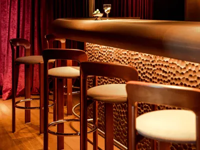 A modern restaurant bar with a wooden counter featuring lit up stools and hanging glasses.