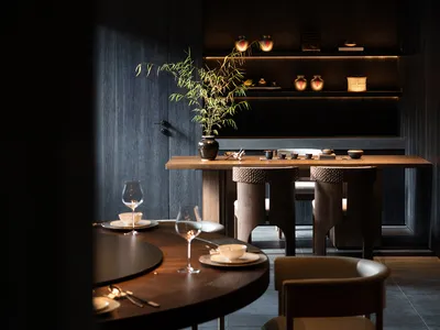 Modern restaurant interior with wooden tables, chairs, and dark, minimalist decor.