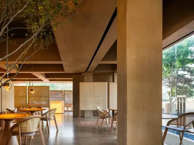 A modern restaurant interior featuring concrete and wooden elements with potted plants.