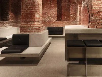 Interior Design of an Industrial Restaurant Bar Featuring Exposed Concrete Walls, Arched Stone Columns, and Bench Seating wit