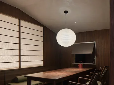 Industrial-style restaurant with a hanging ceiling lamp and wooden furniture, featuring a large window with curtains and a te
