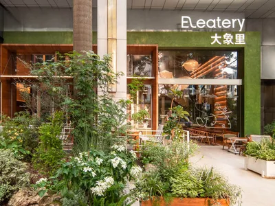 A modern casual cafe with green interiors, made from wood, stone, and glass, featuring a central table and chairs.