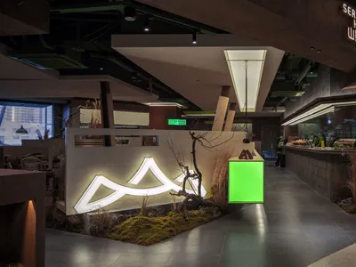 A modern hallway in a restaurant with wooden accents and concrete elements, adorned with plants and illuminated by green scre