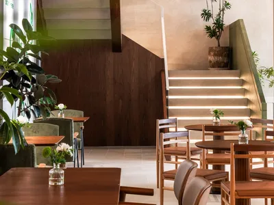 A cozy cafe interior featuring wooden tables and a staircase with plants.