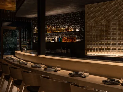 A minimalist restaurant bar interior with wooden seating and stone counter.
