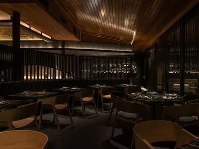 A modern restaurant interior designed with wooden elements, featuring round tables set for dining and a cozy atmosphere.