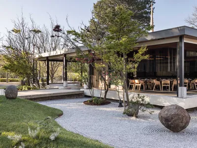A modern restaurant exterior with wooden elements, featuring a pathway and trees.
