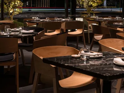 A modern restaurant interior with marble tables and wooden chairs.