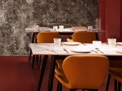 A modern industrial restaurant interior with marble walls and velvet chairs.