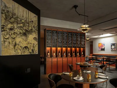 A modern restaurant interior with dark tones, wooden tables, and glass shelves.