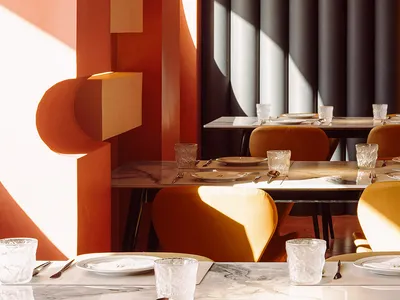 Modern restaurant interior with marble tables, white pendant lights, and orange walls.
