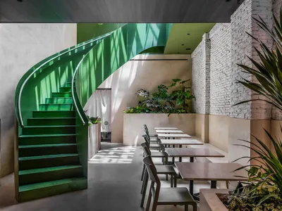 Industrial restaurant interior with concrete walls, brick accents, and a green staircase.