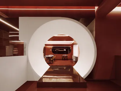 A modern restaurant interior with a large circular door leading into a dining area.